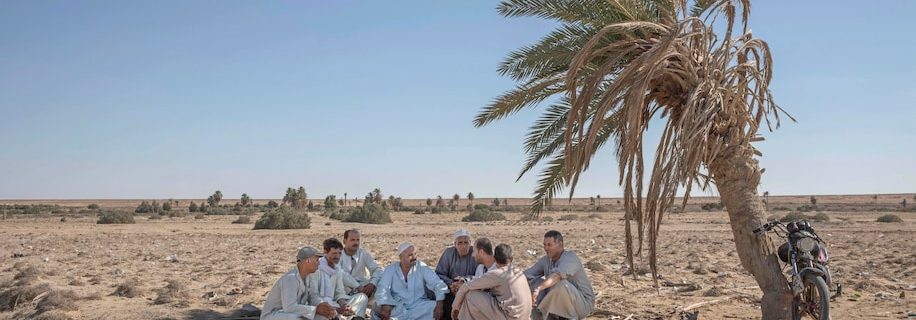 55-year-old Egyptian farmer Makhluf Abu Kassem, center, sits with farmers under shade of a dried up palm tree surrounded by barren wasteland that was once fertile and green, in Second Village, Qouta town, Fayoum, Egypt, Wednesday, Aug. 5, 2020. Abu Kassem fears that a dam Ethiopia is building on the Blue Nile, the Nile’s main tributary, could add to the severe water shortages already hitting his village if no deal is struck to ensure a continued flow of water. “The dam means our death,” he said. (Nariman El-Mofty/Associated Press)